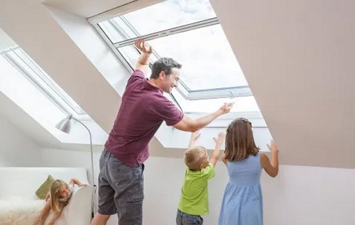 Familie am Dachfenster Ein Mann öffnet ein großes Dachflächenfenster, während zwei Kinder interessiert zuschauen.