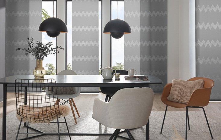 Modernes Wohnzimmer mit Vorhang Modernes Wohnzimmer mit schwarzem Tisch, verschiedenen Stühlen und großen Fenstern, die von grauen Flächenvorhängen bedeckt sind.