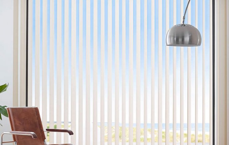 Wohnzimmer mit Lamellenvorhängen Ein hellers Wohnzimmer mit großen vertikalen Lamellenjalousien vor einem Panorama-Fenster.
